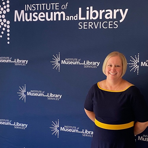 Kristen Sorth stands in front of Institute of Museum and Library Services step and repeat